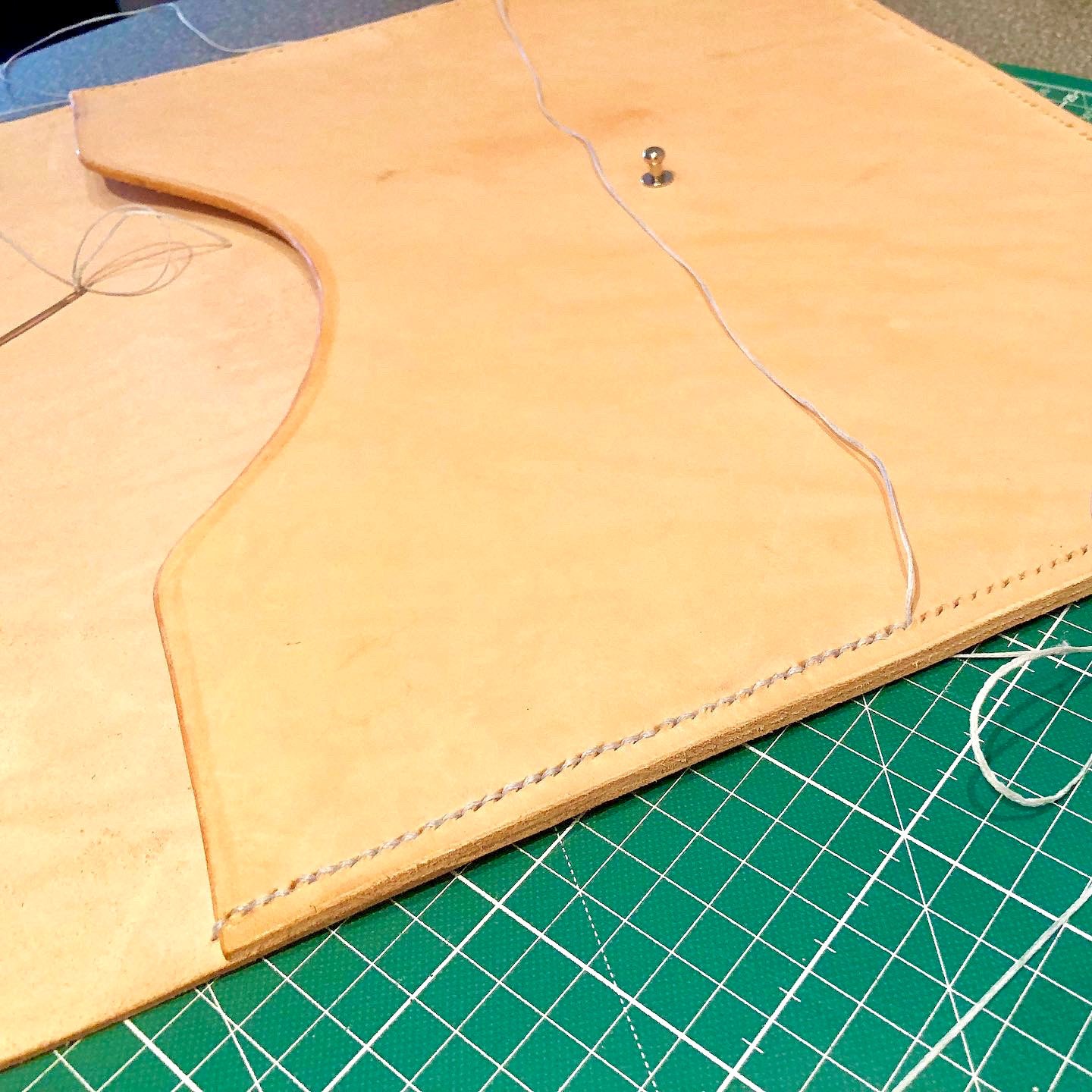 An envelope laptop case by 1985 Studio being stitched by hand on a green cutting mat, needle and thread still in the vegetable-tanned leather