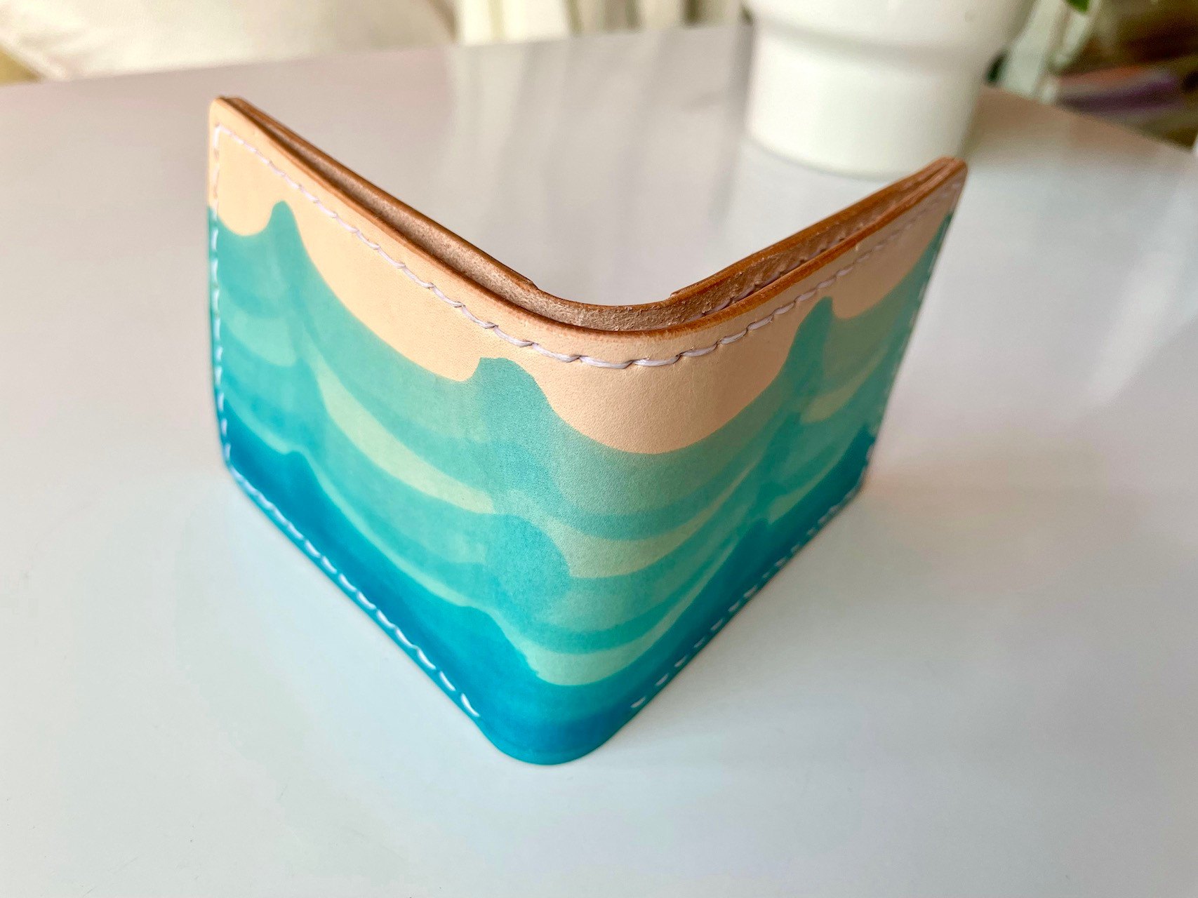 Wave Wallet by 1985 Studio standing half open, its vegetable-tanned leather dyed in waves of turquoise and blue on the outside and stitched in white thread