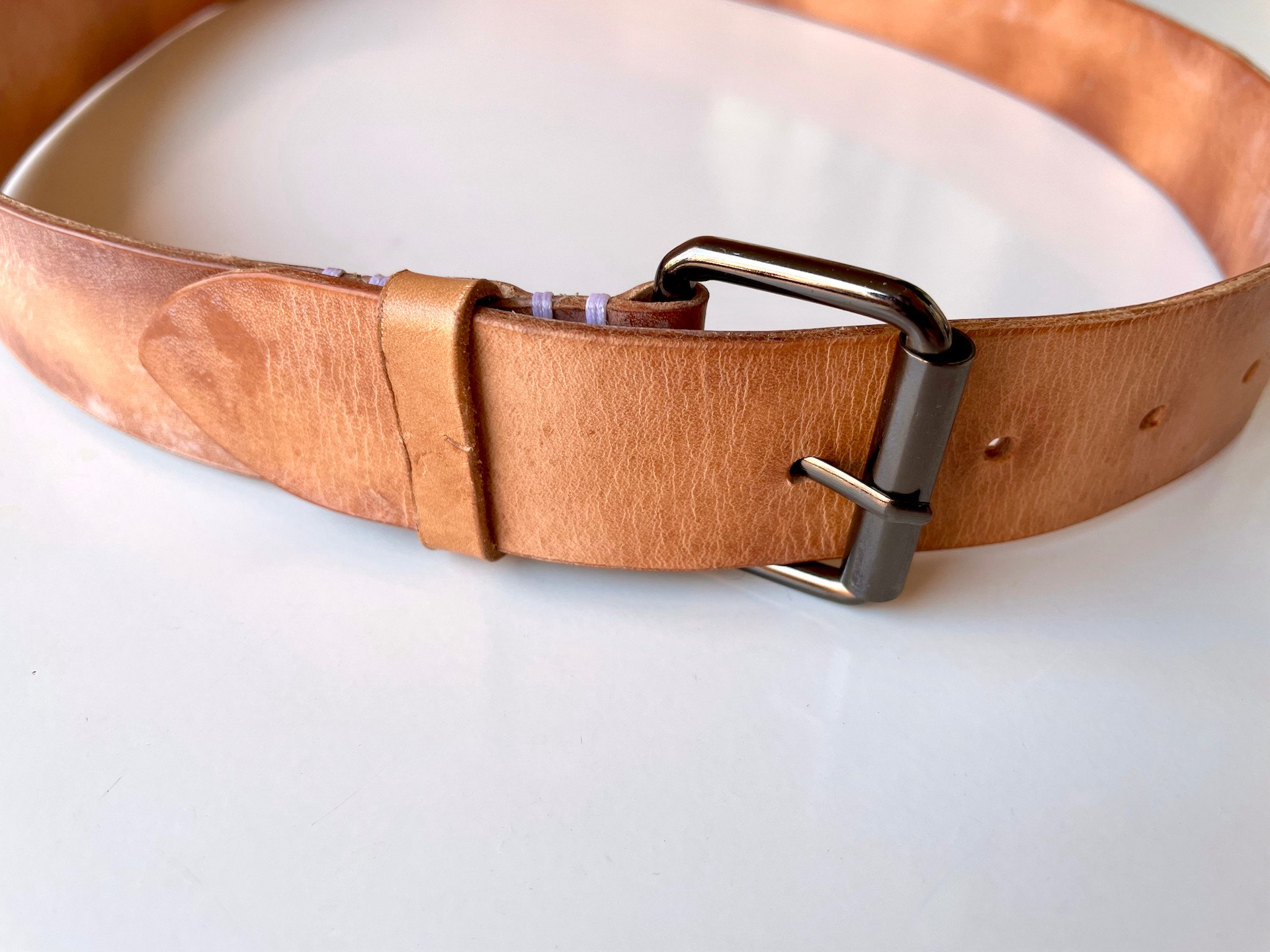 Roller buckle belt by 1985 Studio buckled, its end through the gunmetal buckle and the keeper, the vegetable-tanned leather marked with patina