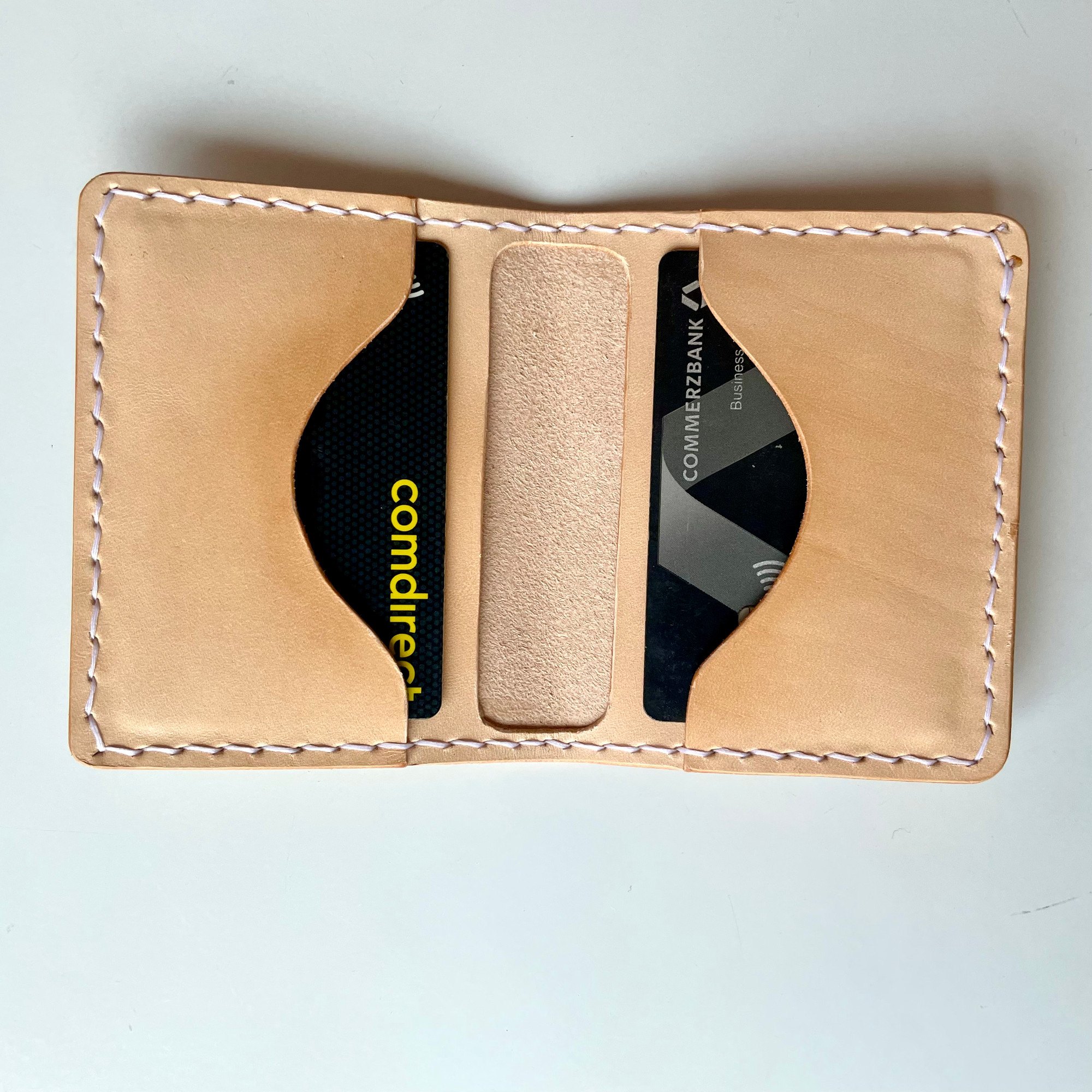 AirTag card wallet by 1985 Studio lying open, a card in each of its two slots with curved cut-outs, the vegetable-tanned leather stitched in white around the edge