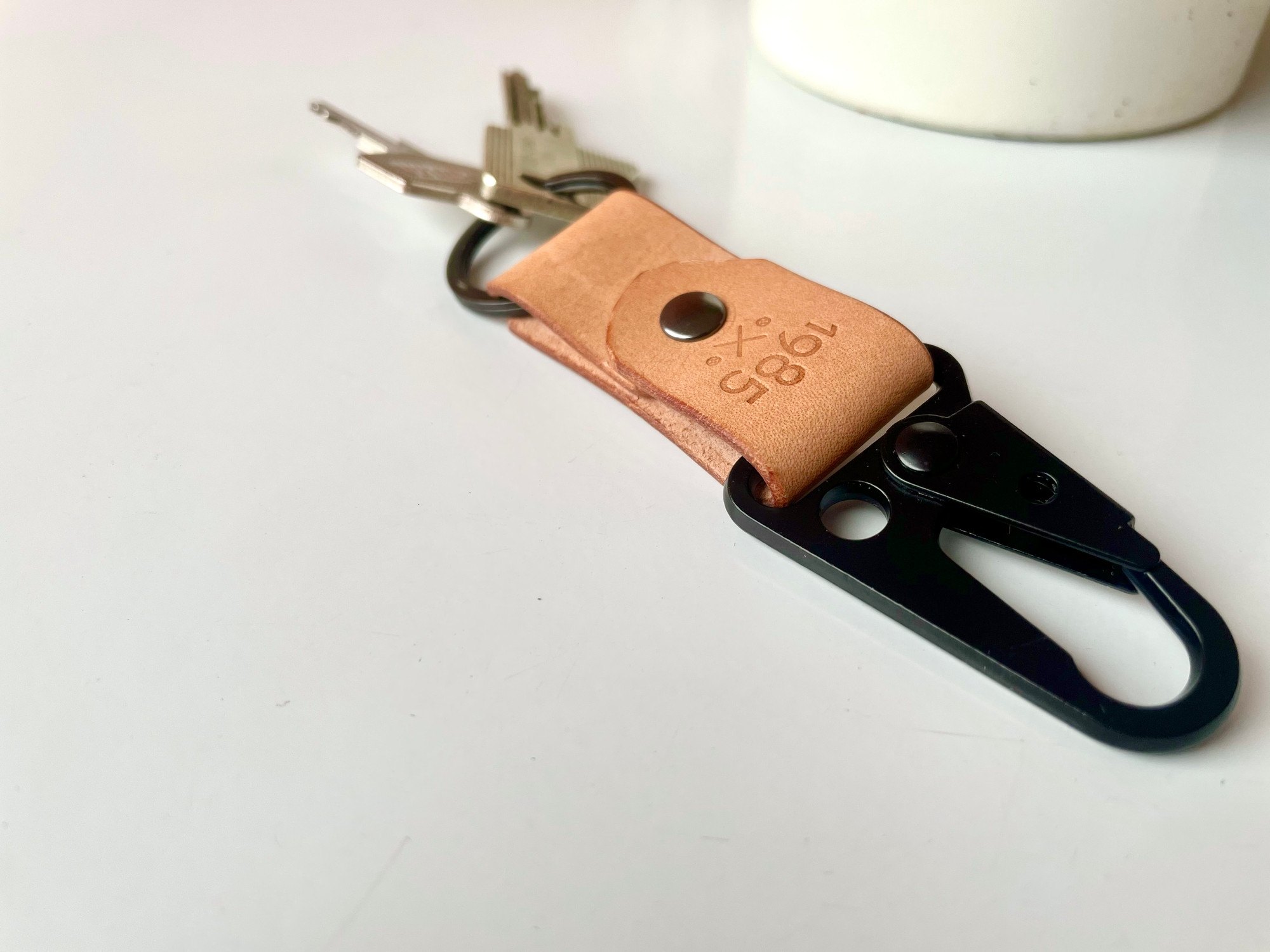 Carabiner keychain by 1985 Studio with keys on its split ring, the black clip in front and the 1985 mark stamped into the vegetable-tanned leather