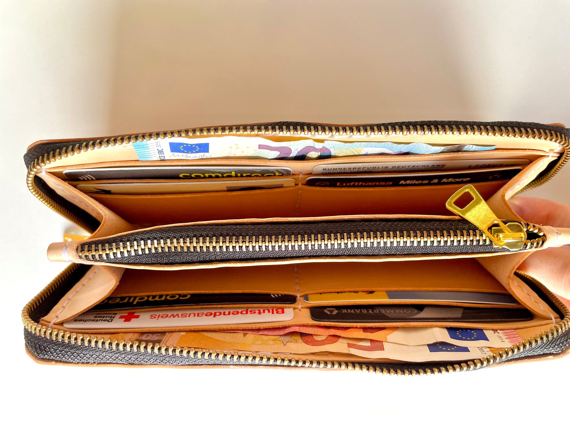 Zip-around long wallet by 1985 Studio held open, cards in its slots of vegetable-tanned leather and banknotes in the pockets on both sides of the coin pocket