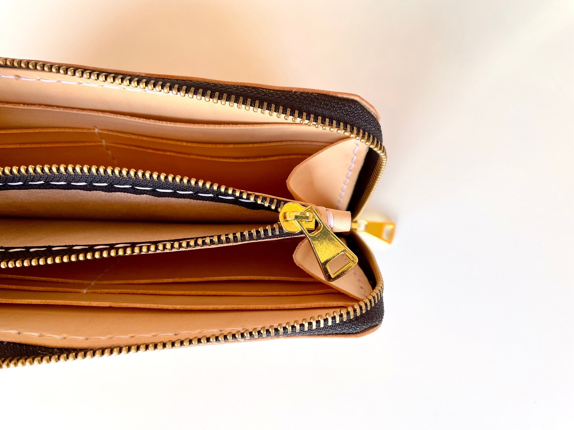Zip-around long wallet by 1985 Studio open from above, the pull of the coin pocket between rows of card slots in vegetable-tanned leather