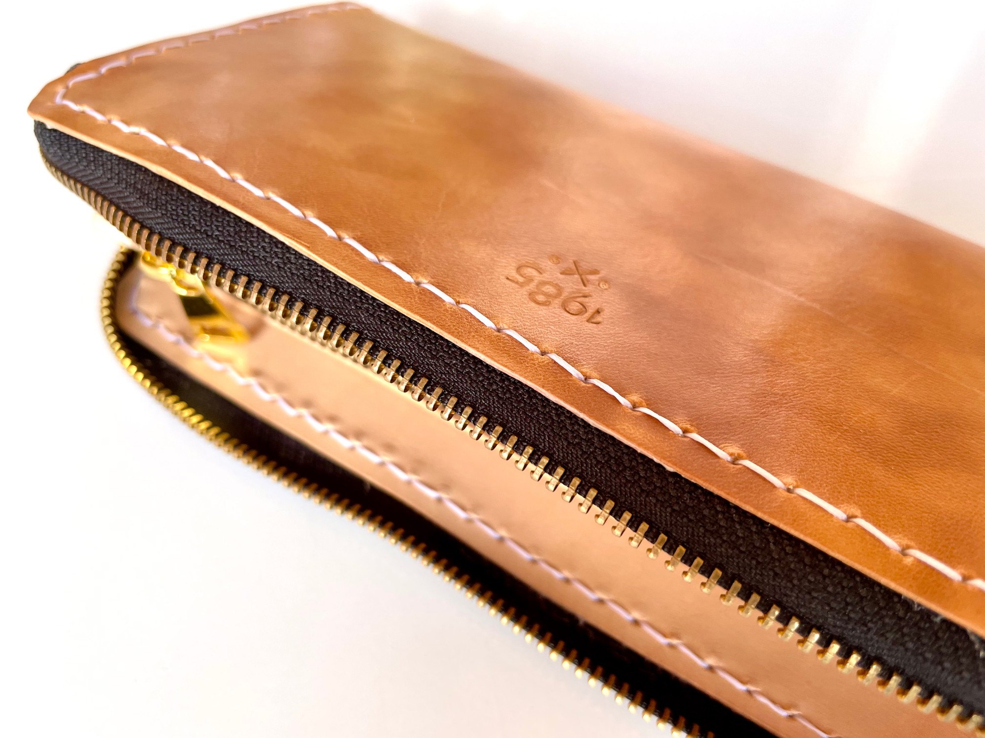 The 1985 mark stamped into the hot-stuffed shell of a long wallet by 1985 Studio, vegetable-tanned leather inside, its zip running along the stitched edge