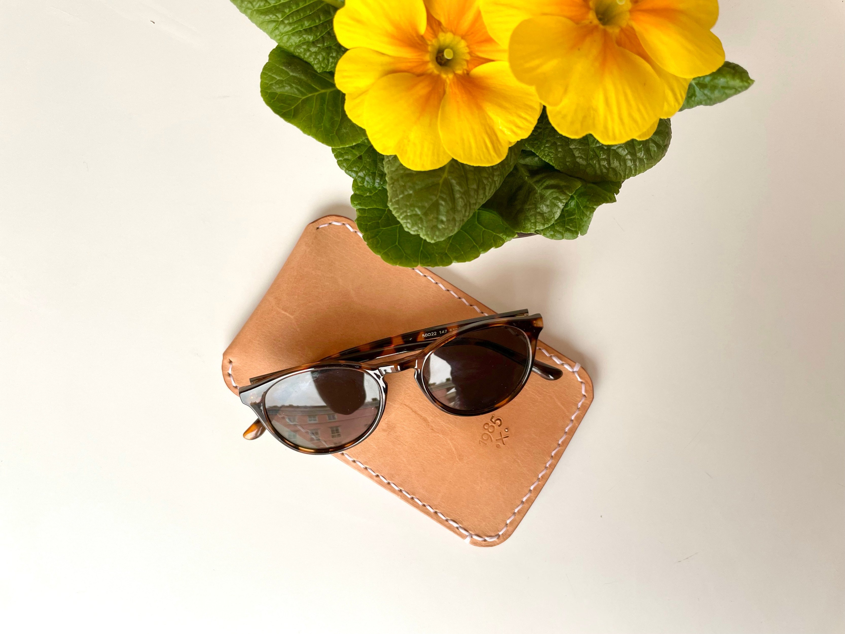 Slim sunglasses pouch by 1985 Studio in vegetable-tanned leather, saddle-stitched by hand in pale thread and stamped with the 1985 mark, sunglasses resting on top