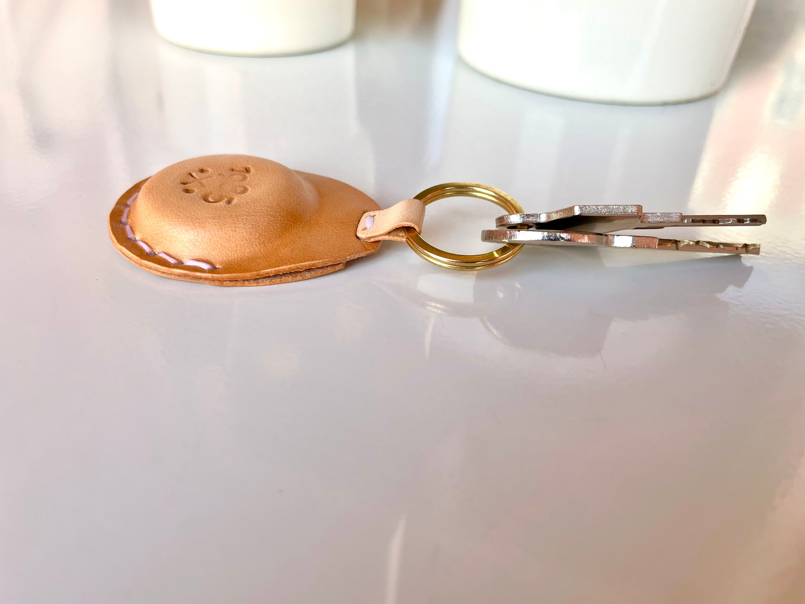AirTag key fob by 1985 Studio from the side, its vegetable-tanned leather domed over the AirTag and stitched along the edge, keys on the brass ring