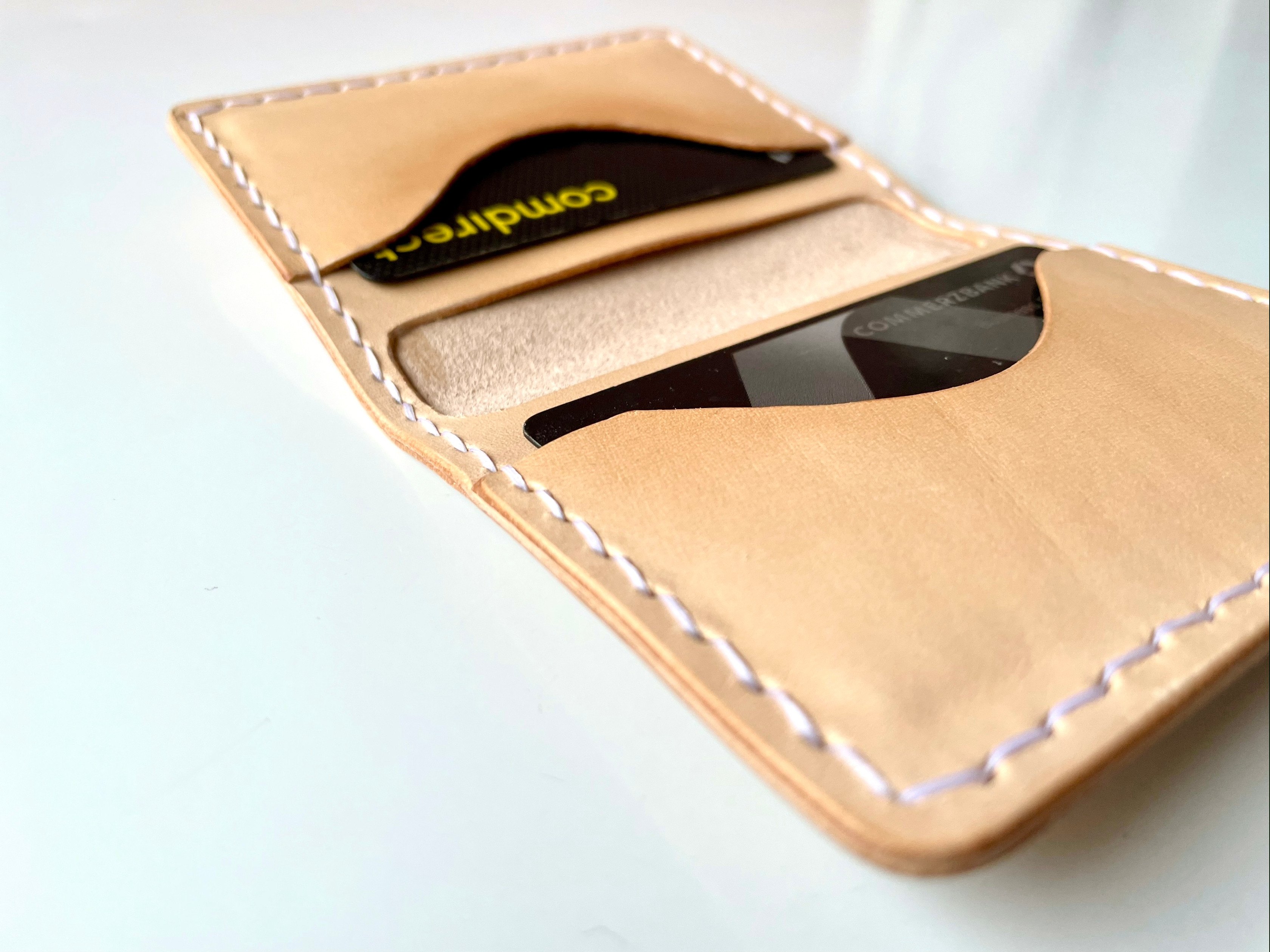 AirTag card wallet by 1985 Studio open at an angle, two bank cards in its slots and the flesh side of the vegetable-tanned leather between them