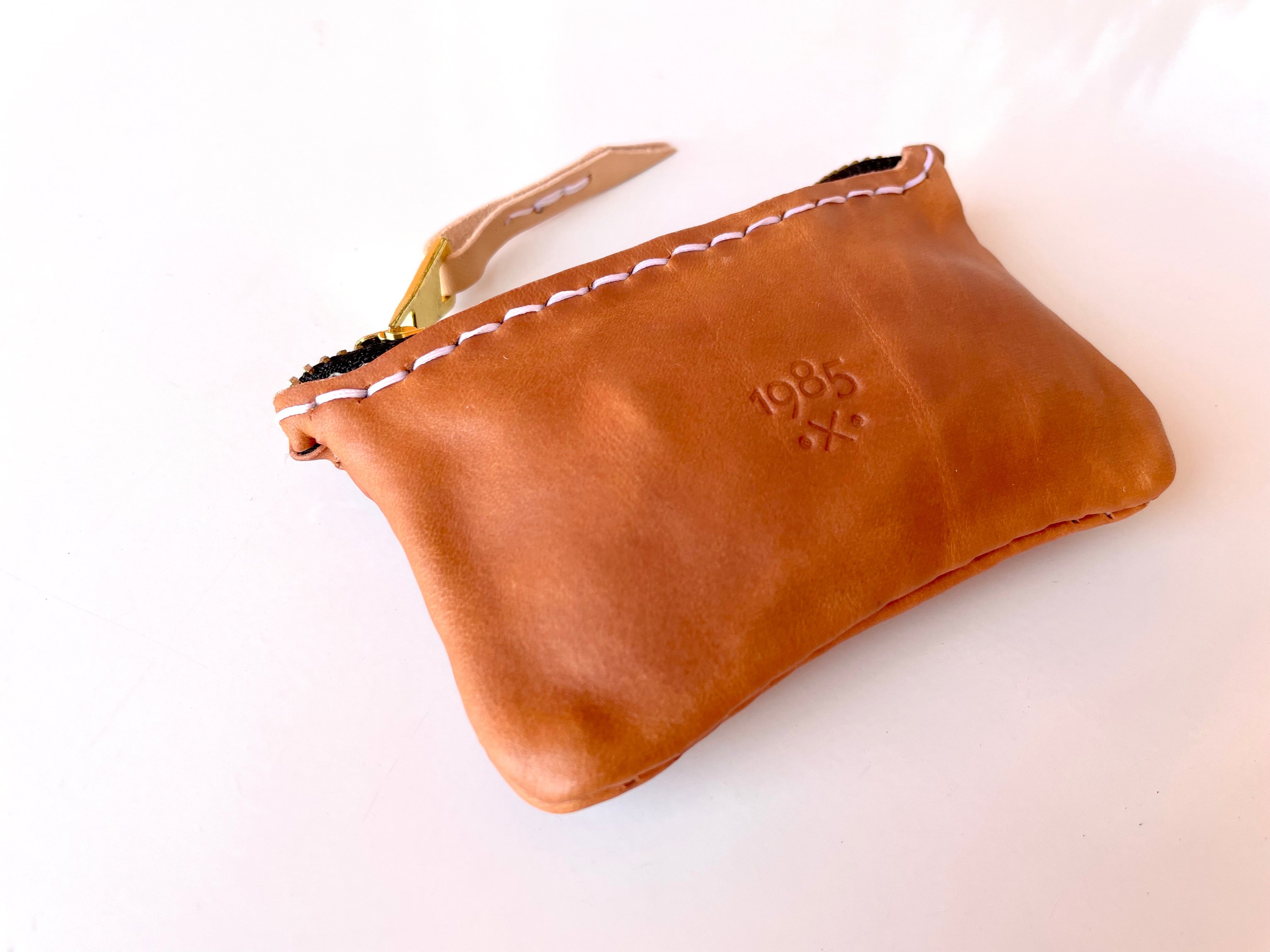 Car key pouch by 1985 Studio up close, the 1985 mark stamped into its cognac vegetable-tanned leather, white stitches along the top and a leather tab on the zip pull