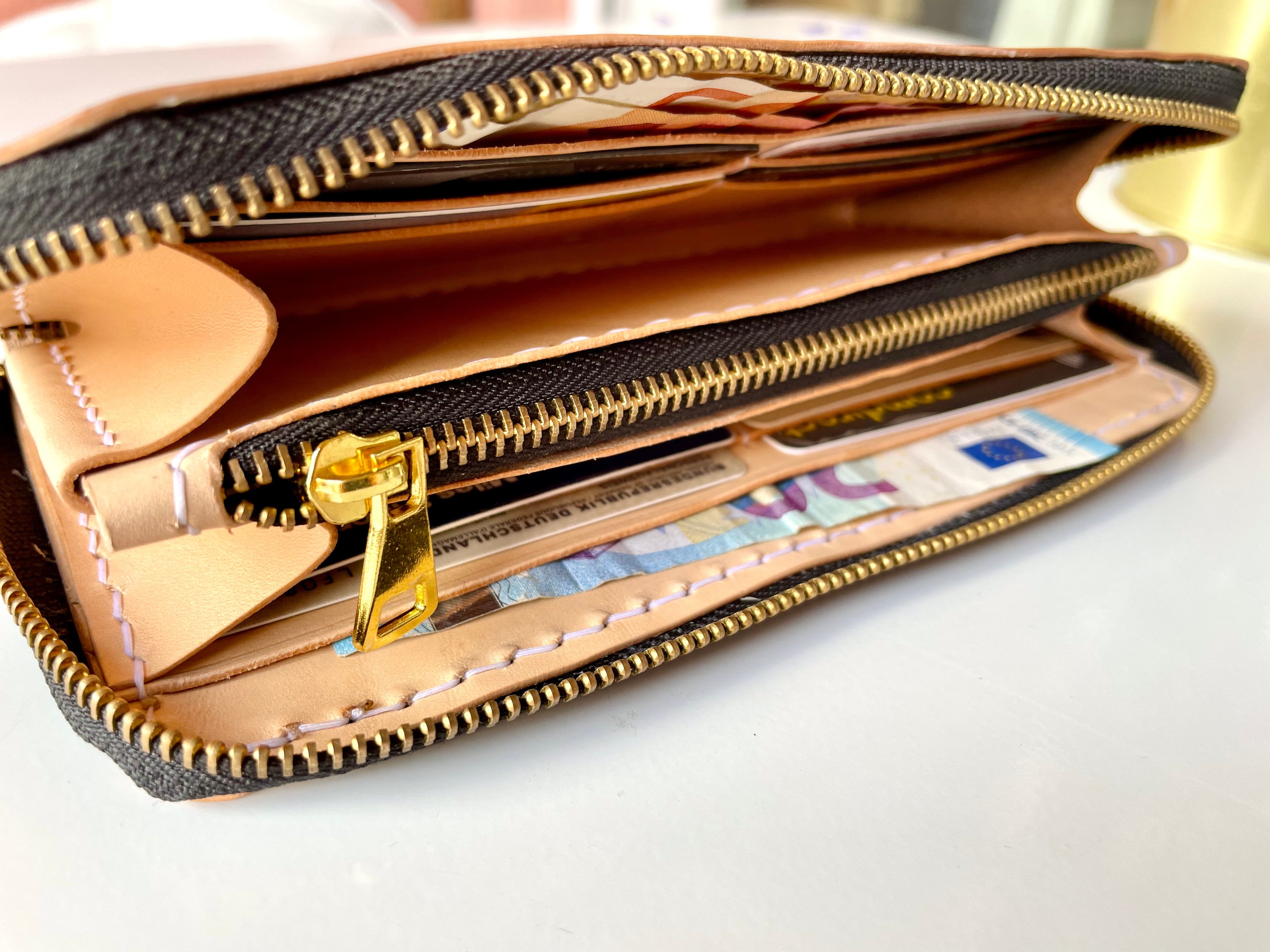 Zip-around long wallet by 1985 Studio open at an angle, its gold-colored zip around the edge, card slots of natural vegetable-tanned leather and a zipped coin pocket in the middle