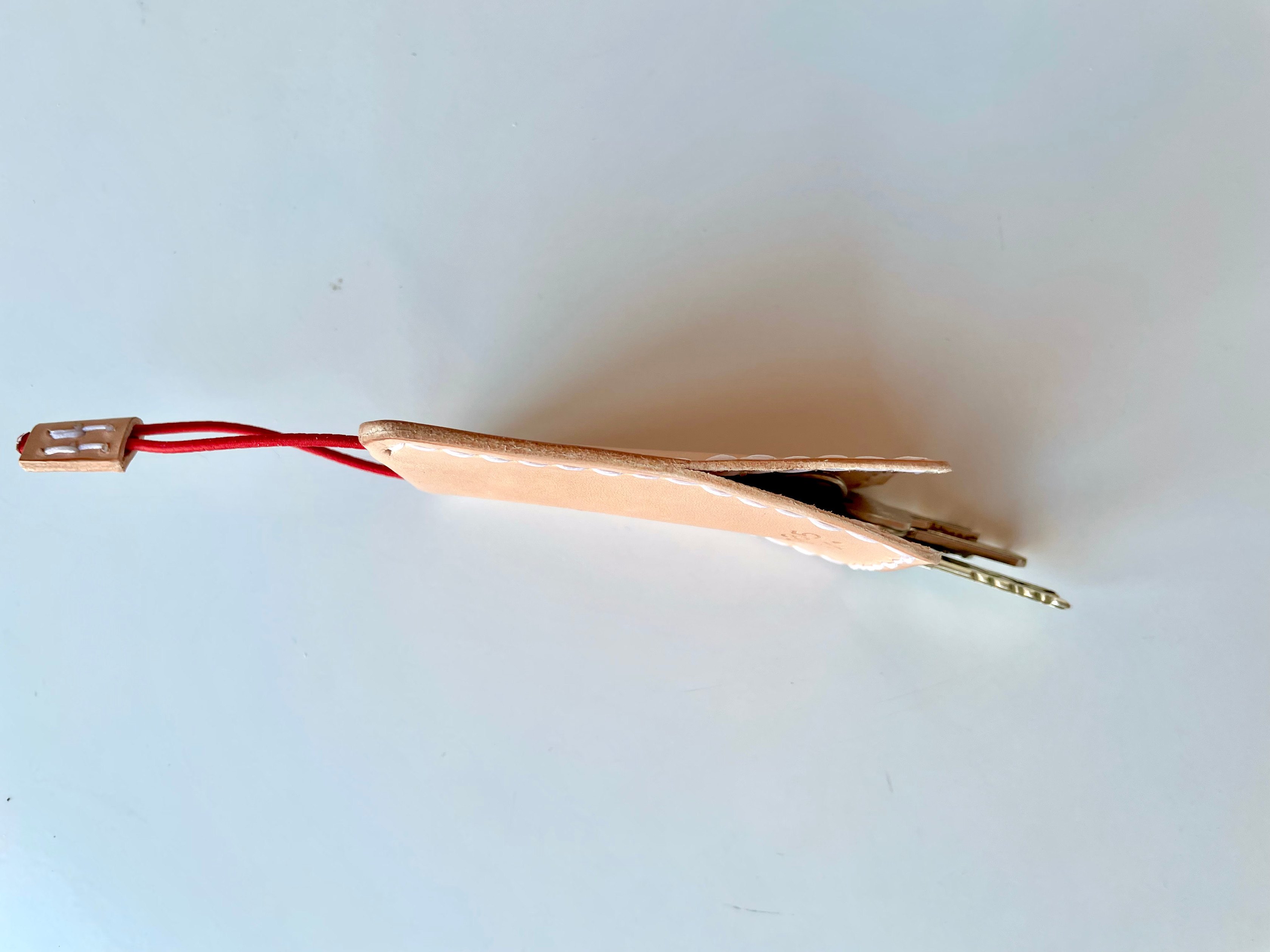 Slim key case by 1985 Studio in vegetable-tanned leather, flat on the table from the side, the red cord and its leather tab at one end and keys at the other